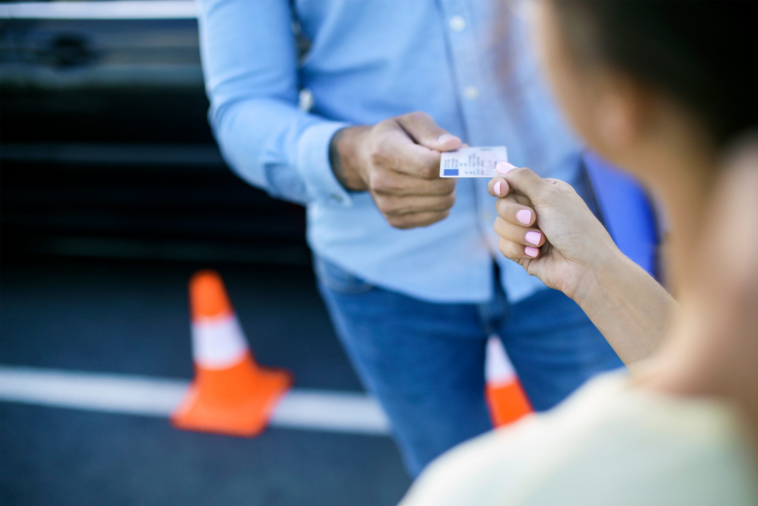 Passage d'examin du permis de conduire, un homme en chemise tant le permis a une femme qu'on apperçoit de dos.