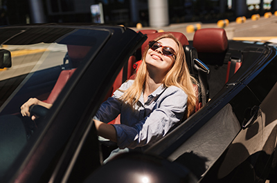 Jeune femme blonde avec des lunettes de soleil est au volant d'une voiture décapotable