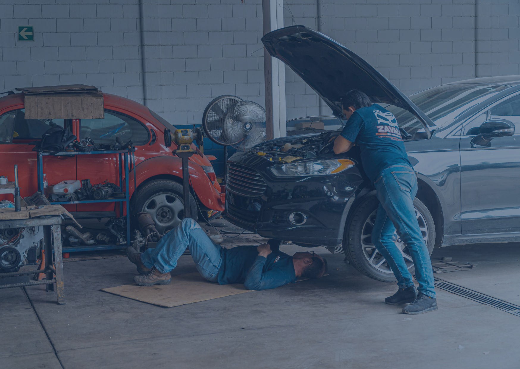 Le capot d'une voiture est ouvert, 2 garagistes sont en train de faire les réparation sur le véhicule